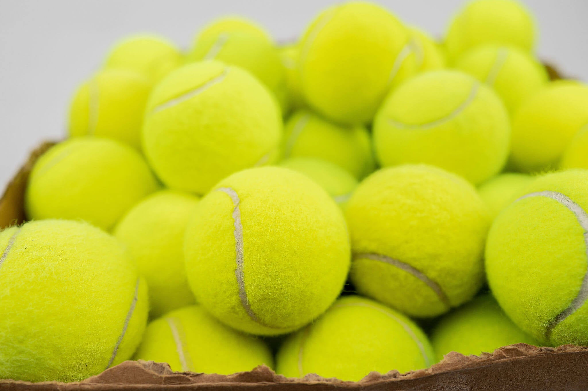 A dog licking peanut butter from a jar over a bowl of kibble against an orange background.